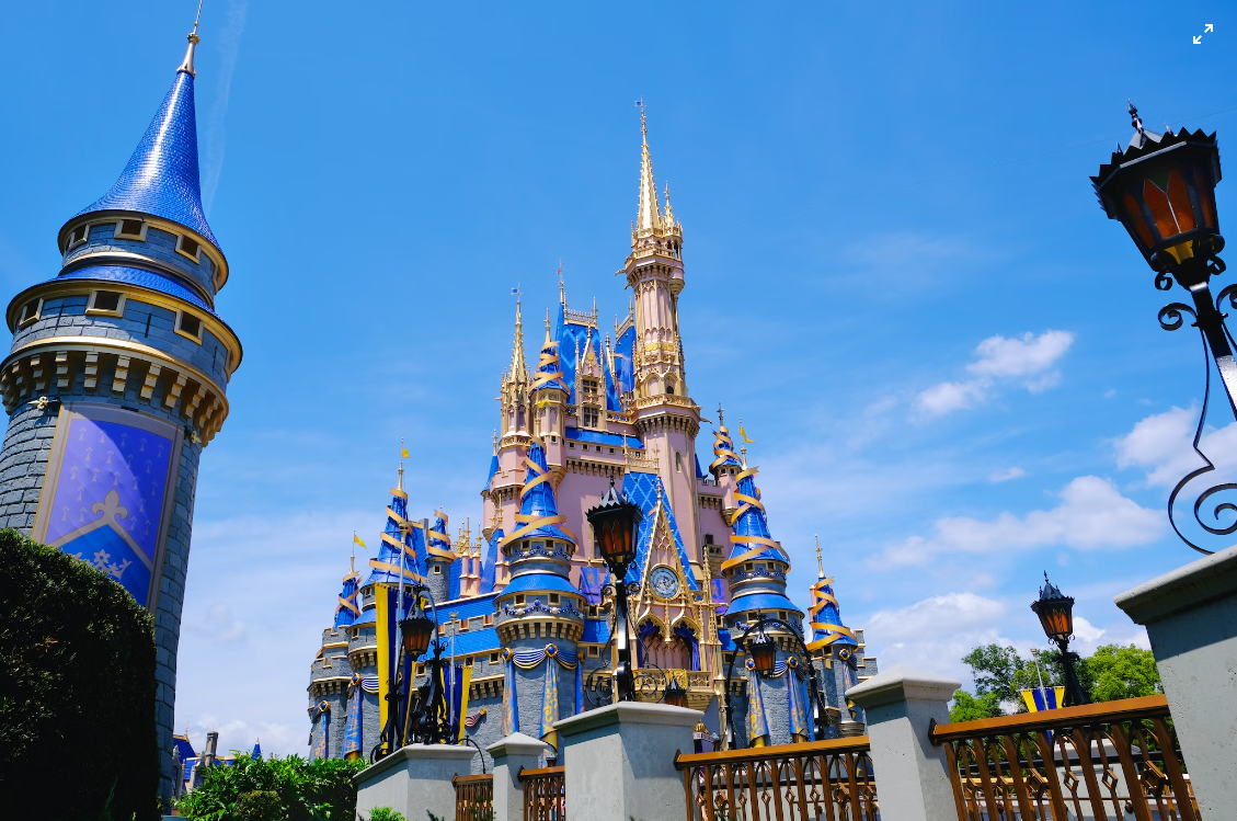  A fairytale castle with ornate, blue and gold turrets against a clear blue sky, evoking a sense of magic and wonder, possibly within a theme park setting.
